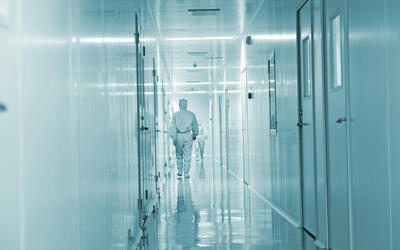 Stock image of a person in white protective clothing walking down a white corridor. Our strand of AnNex included analysis of images of science in public.